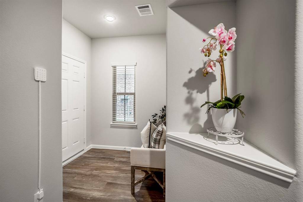 Looking back toward the front door, you’ll spot the Ring security control panel just inside, as well as a tall window that adds extra natural light to the foyer. The recessed display shelf stands out here—an ideal spot for seasonal décor or personal touches. Just out of frame to the left is the door to the garage, making this hallway as functional as it is stylish.