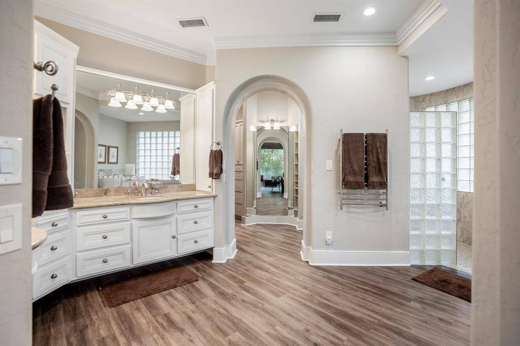 The primary bath is elegantly designed with dual vanities featuring a storage tower for toiletries & appliances, a full-length mirror adds a boutique feel, and the stylish shower features glass block privacy and a no-threshold entry.