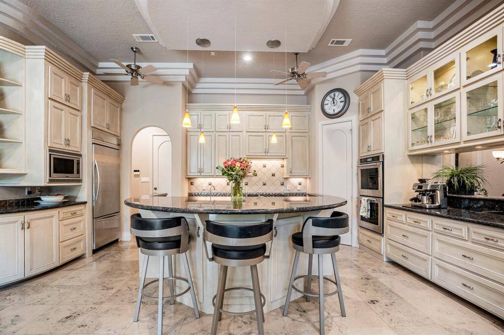 The kitchen's soothing color palette is beautifully accented by a darker granite island and counters, complemented by large format marble floors, with cabinets and drawers with soft-close mechanisms, display shelves, and a walk-in pantry for optimal storage and effortless organization completing the sophisticated design.