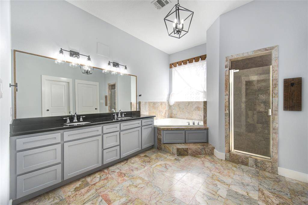 The spa-like en-suite bathroom is designed for relaxation, boasting a dual vanity with granite countertops, a luxurious soaking tub, and a separate walk-in shower with sleek tile finishes.