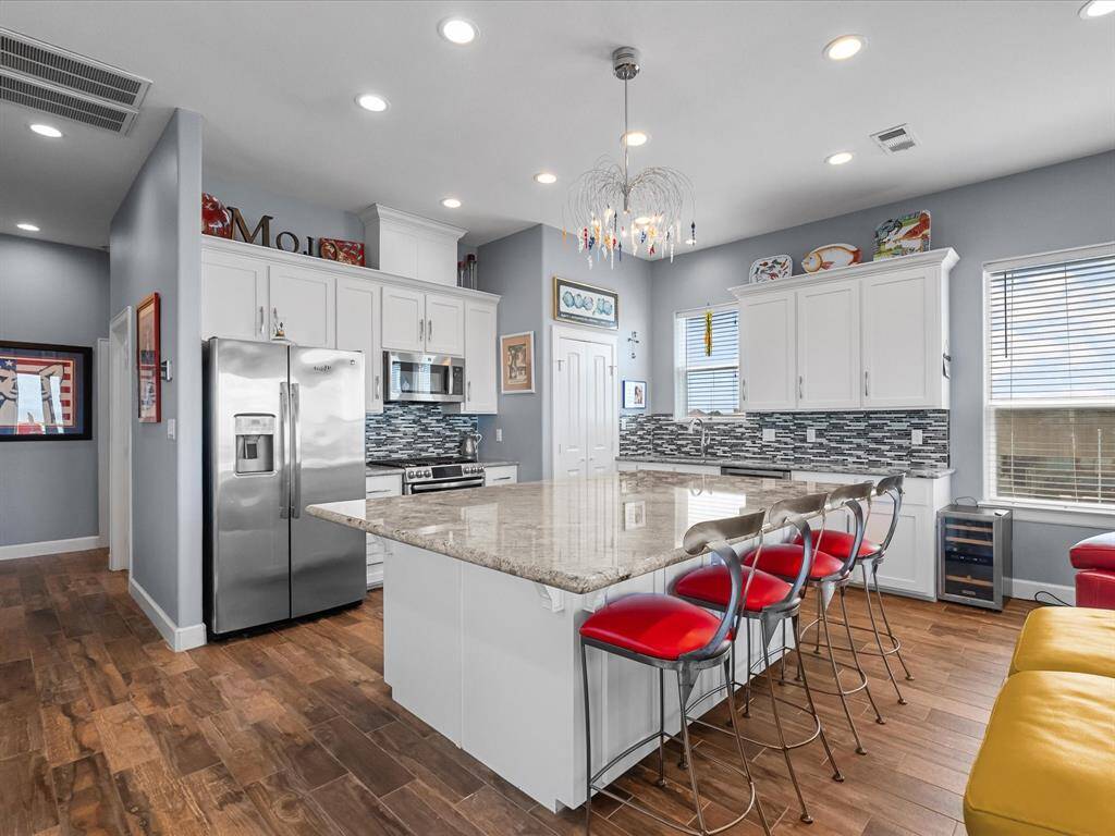 This modern kitchen features custom cabinets, sleek stainless steel appliances, a spacious granite island and stylish backsplash. The open layout is complemented by ample natural light and contemporary lighting fixtures, creating an inviting and functional space.