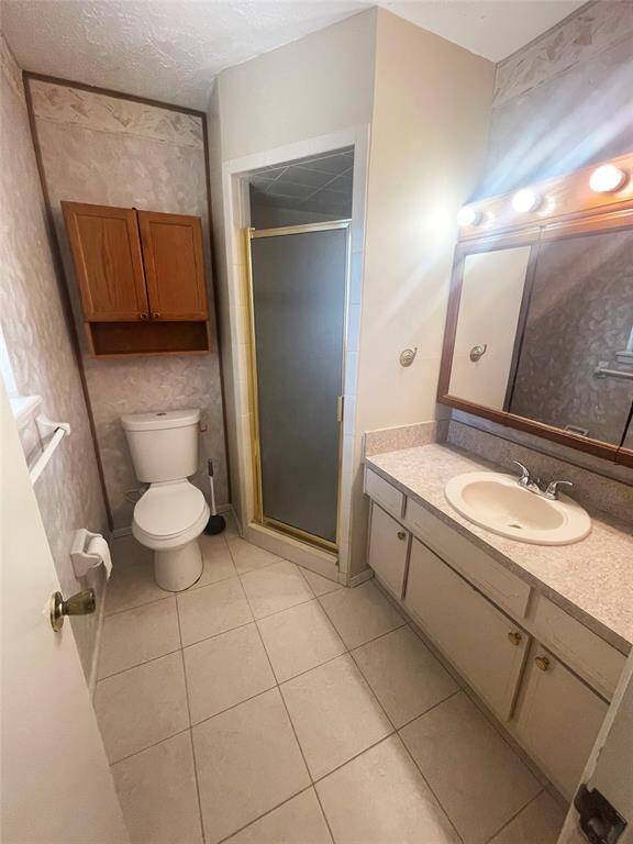 This bathroom features a single sink vanity with a large mirror, a toilet, and a walk-in shower with a glass door. It has tile flooring, a wall-mounted cabinet for storage, and neutral-colored walls.