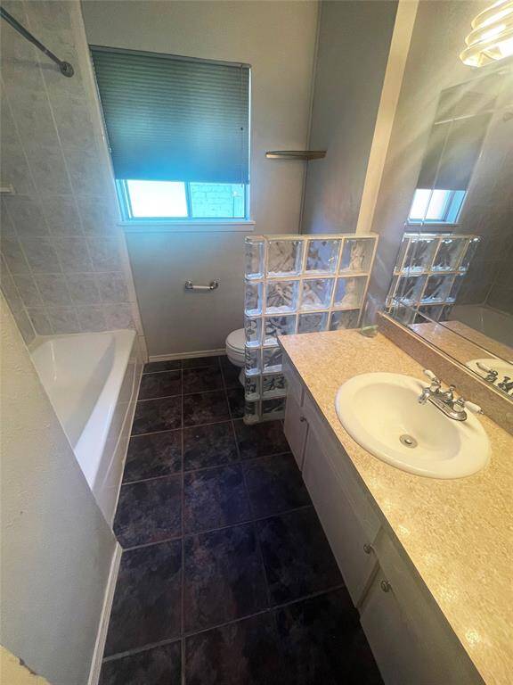This bathroom features a tiled floor, a bathtub with a tiled surround, and a single sink vanity with a mirror. A glass block partition adds a modern touch, and a window provides natural light.