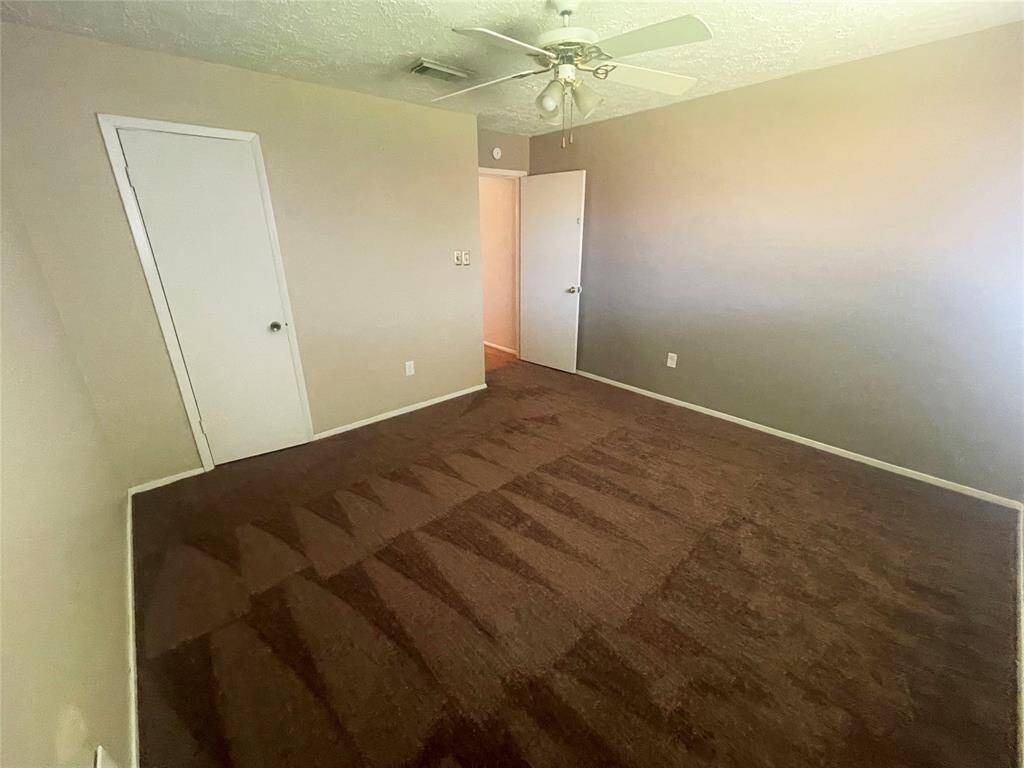 This room features neutral walls, brown carpet, a ceiling fan, and two doors, offering a cozy and functional space.