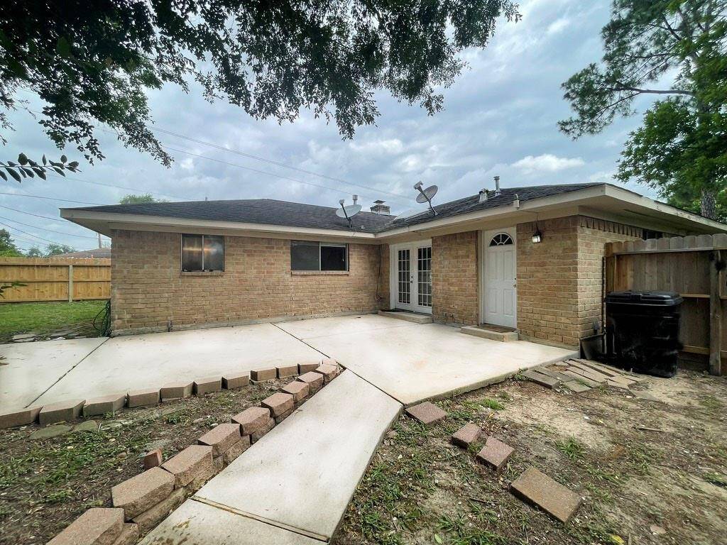 This photo showcases the backyard of a single-story brick home featuring a spacious concrete patio, bordered by a wooden fence and surrounded by trees, offering a private outdoor area ideal for relaxation or entertaining.