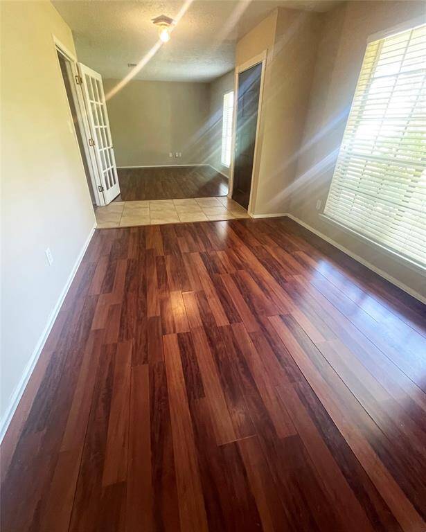 This room features rich wood flooring, a large window with blinds for natural light, and a transition to a tiled area. French doors lead to an adjacent space, providing an open and versatile layout.