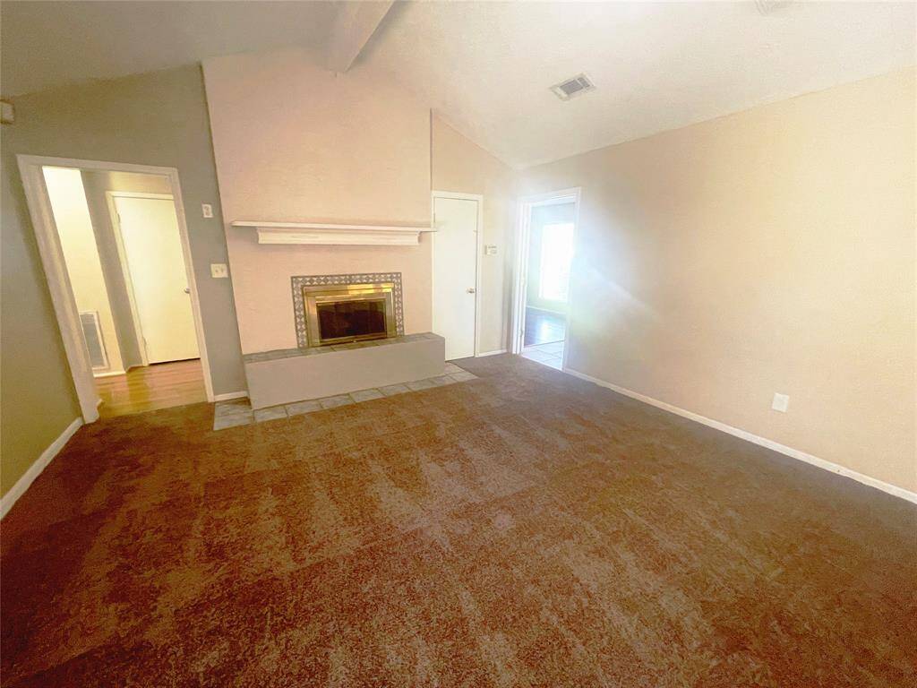This room features a cozy fireplace with a mantel, complemented by carpeted flooring and neutral-toned walls. It has a high ceiling, adding to the spacious feel, with doorways leading to other areas of the home.