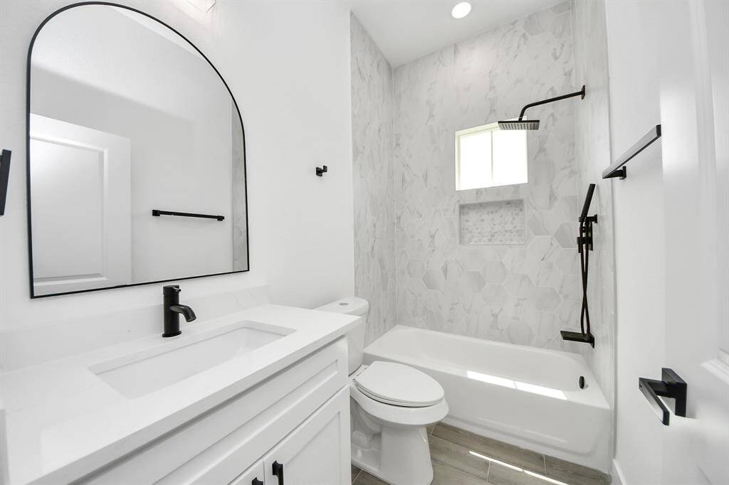 Bright and stylish secondary bath featuring matte black fixtures, a soaking tub with rain showerhead, and elegant geometric tile surround.