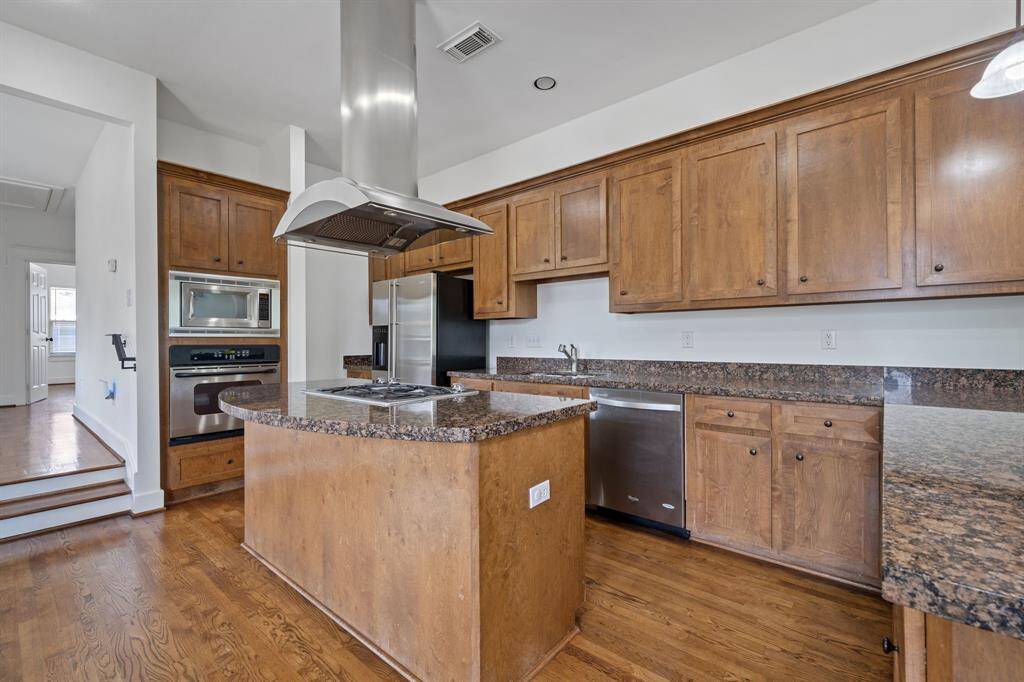 This beautiful kitchen features a large island with cooktop, stainless steel appliances, an abundance of beautiful wood cabinetry, and granite countertops.