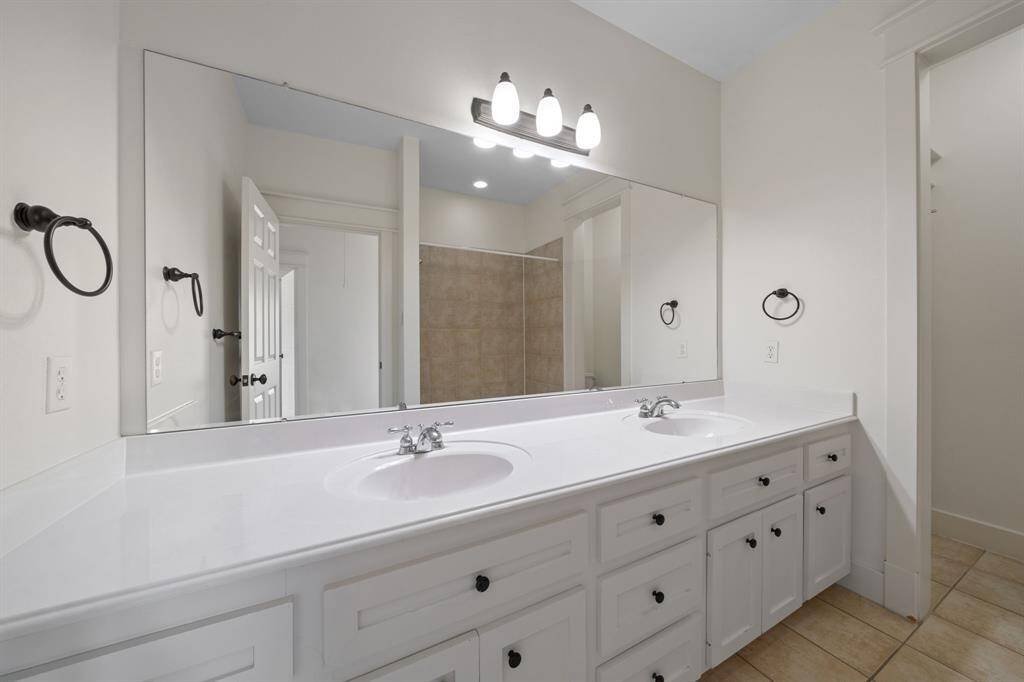 Spacious secondary bathroom featuring white cabinets, granite countertops, double sinks, a large mirror and vanity lights.