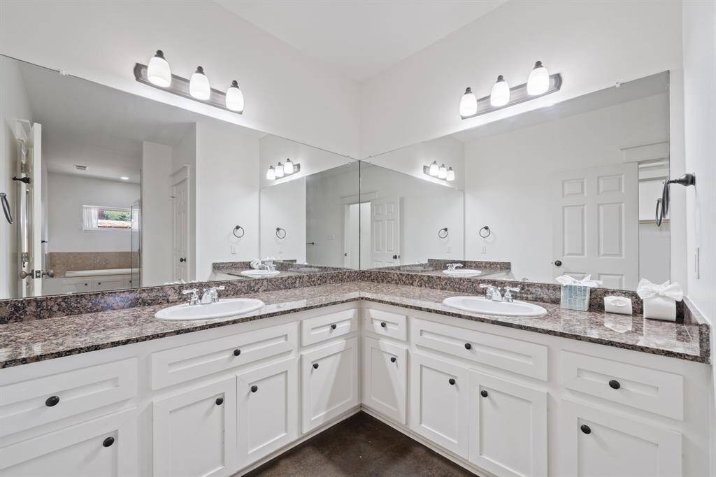 Primary Bathroom, featuring white cabinetry, granite countertops, vanity lights, and his/her sinks with modern finishes.