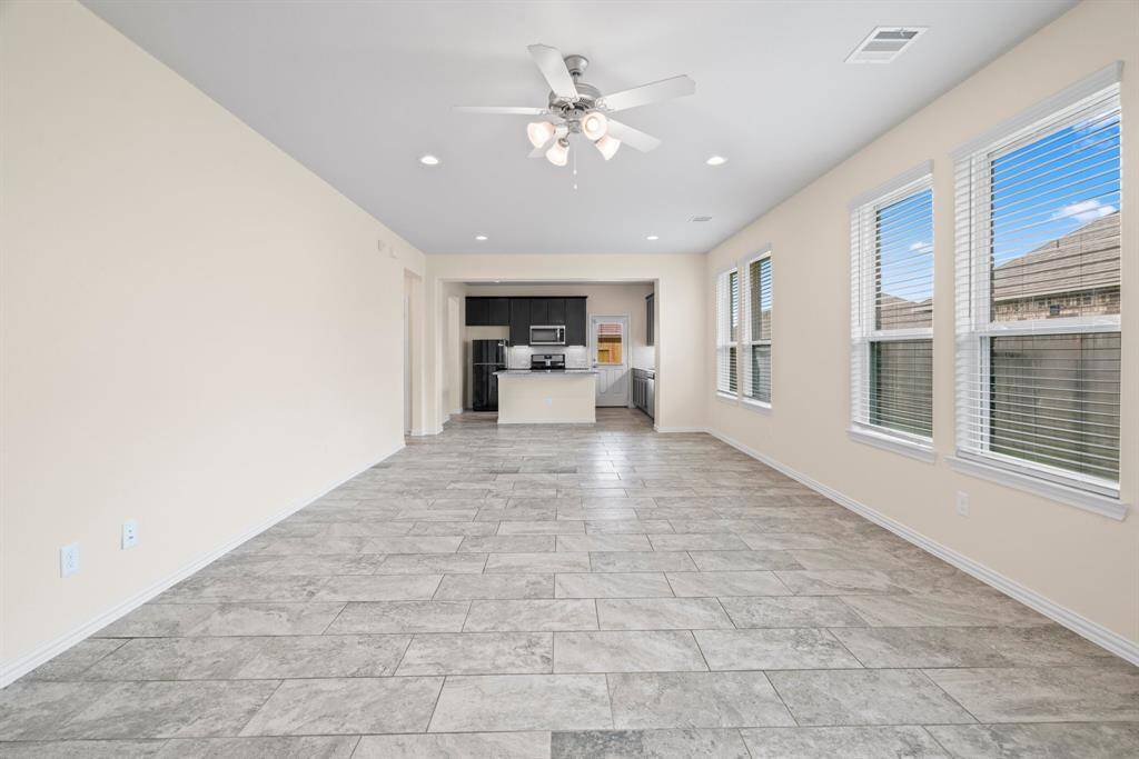 Open-plan area features modern tile flooring, ample natural light from large windows, and a ceiling fan. It seamlessly connects to a sleek kitchen with dark cabinetry and stainless-steel appliances, offering a welcoming atmosphere for living and dining.