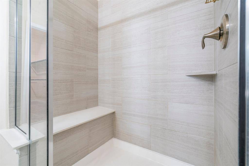 This bathroom features a clean, modern design with a tiled shower and bathtub, sleek dark cabinetry, a wide mirror, and neutral-colored walls.