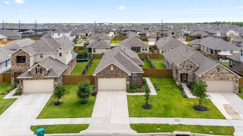 Modern brick home with a welcoming front entrance. It features a wooden door with a glass panel, surrounded by well-maintained landscaping and a wooden fence. The property offers a neat walkway and lush green grass, creating an inviting curb appeal.