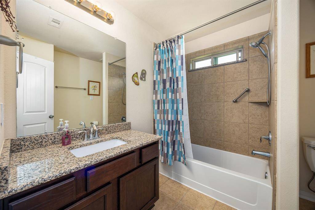 Secondary bath features tile flooring, bath/shower combos with tile surround, dark wood cabinets and beautiful granite countertops