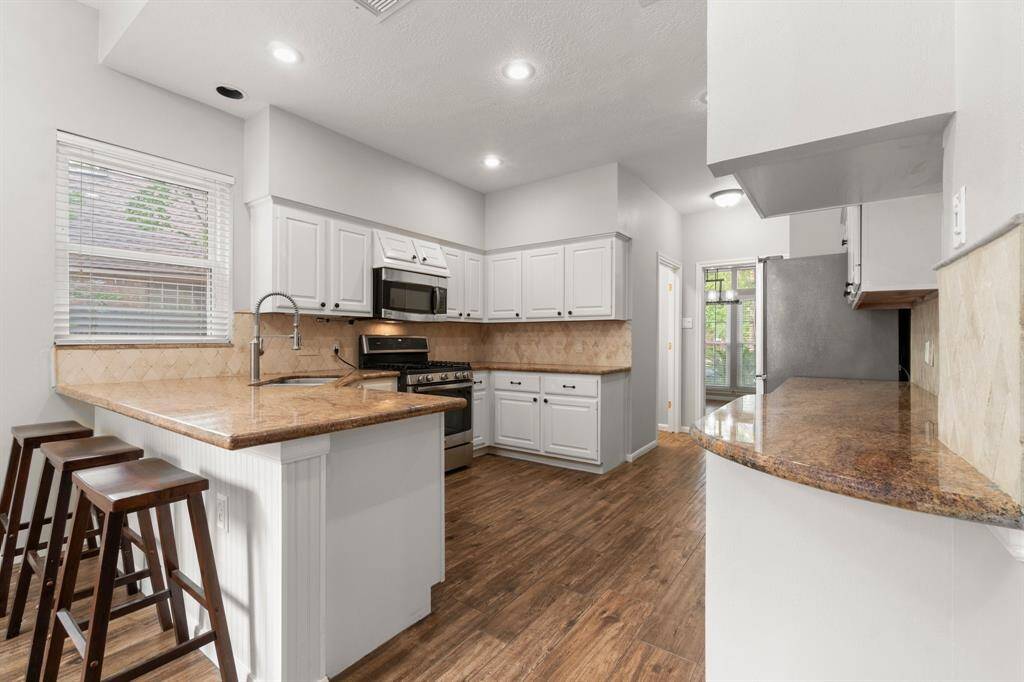 This kitchen features spacious white cabinetry,  and a stylish granite countertop with a breakfast bar. The wood flooring and ample lighting create a warm and inviting atmosphere.