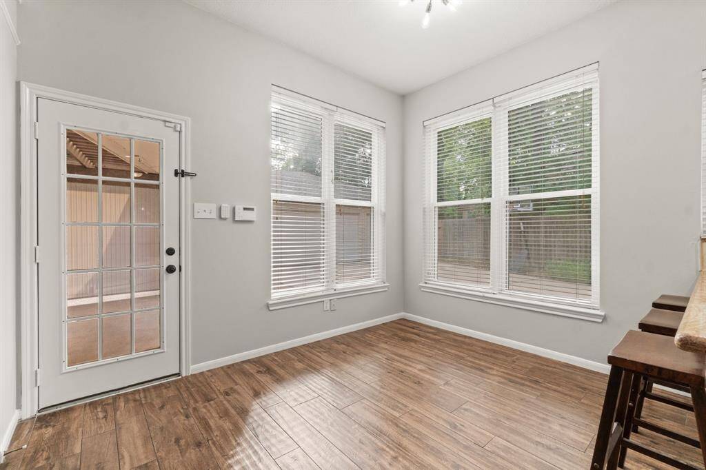 Bright, airy breakfast nook with large windows and a stylish glass door opening to the patio. Features wood-like flooring and a cozy bar area with seating. Ideal for morning coffee or casual meals.