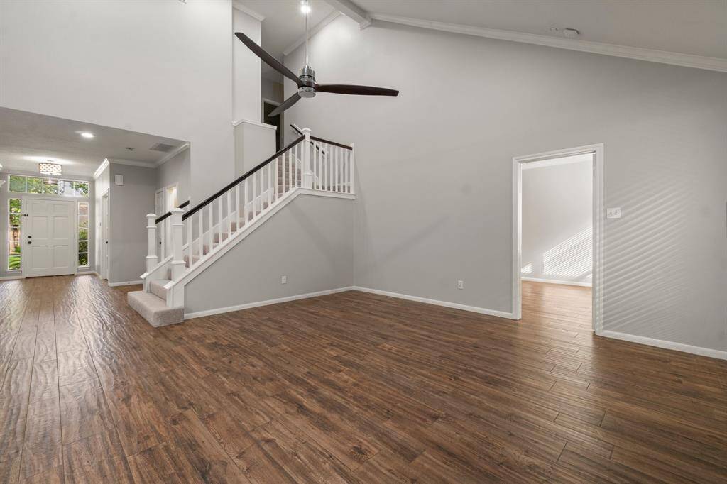 This expansive interior offers an open-concept layout seamlessly connecting the kitchen and living area, all enhanced by warm wood flooring. The kitchen is equipped with sleek granite countertops, contemporary appliances, and a convenient breakfast bar with seating. A stylish staircase leads upstairs, while a ceiling fan adds to the light and breezy ambiance.