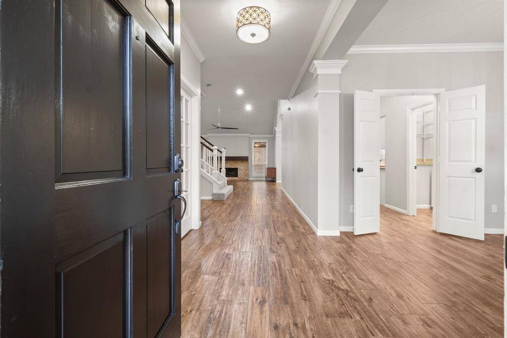 Welcoming entryway with a dark wooden door opening to a bright, spacious entryway featuring wood flooring, a neutral color palette and architectural details that create an inviting and modern atmosphere..