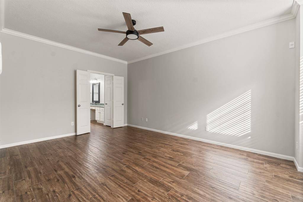 This generously sized room boasts wood-look flooring, soft neutral walls, and a contemporary ceiling fan. Double doors open to an en-suite bathroom with dual vanities, enhancing the bright and open feel—perfect for a serene primary retreat.