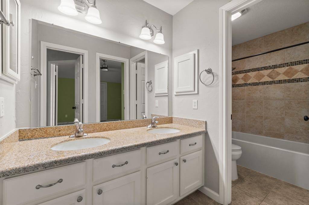 This spacious living area features high ceilings, hardwood floors, a modern ceiling fan, and a cozy fireplace, visible from a carpeted staircase. Large windows provide ample natural light.