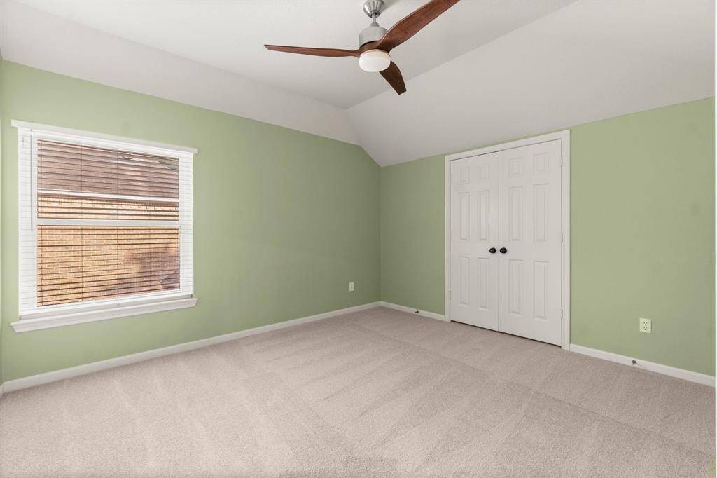 This room features a soft green paint and beige carpet, offering a tranquil atmosphere. It includes a ceiling fan for added comfort and a window with blinds for natural light. There's a double-door closet for storage, making it a practical space.