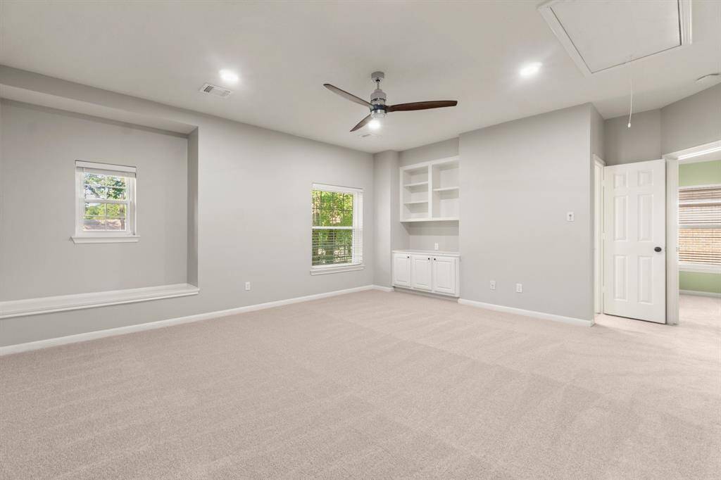 This spacious gameroom features soft carpet, neutral gray walls, and built-in shelving with cabinetry. It includes a ceiling fan and recessed lighting, creating the perfect atmosphere for multiple uses.