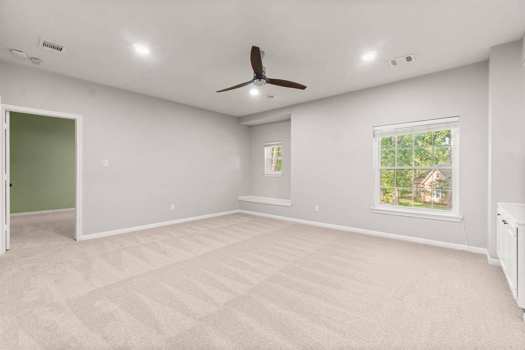 A large window offers a view of greenery, while the room also connects to another carpeted space, enhancing its versatility.