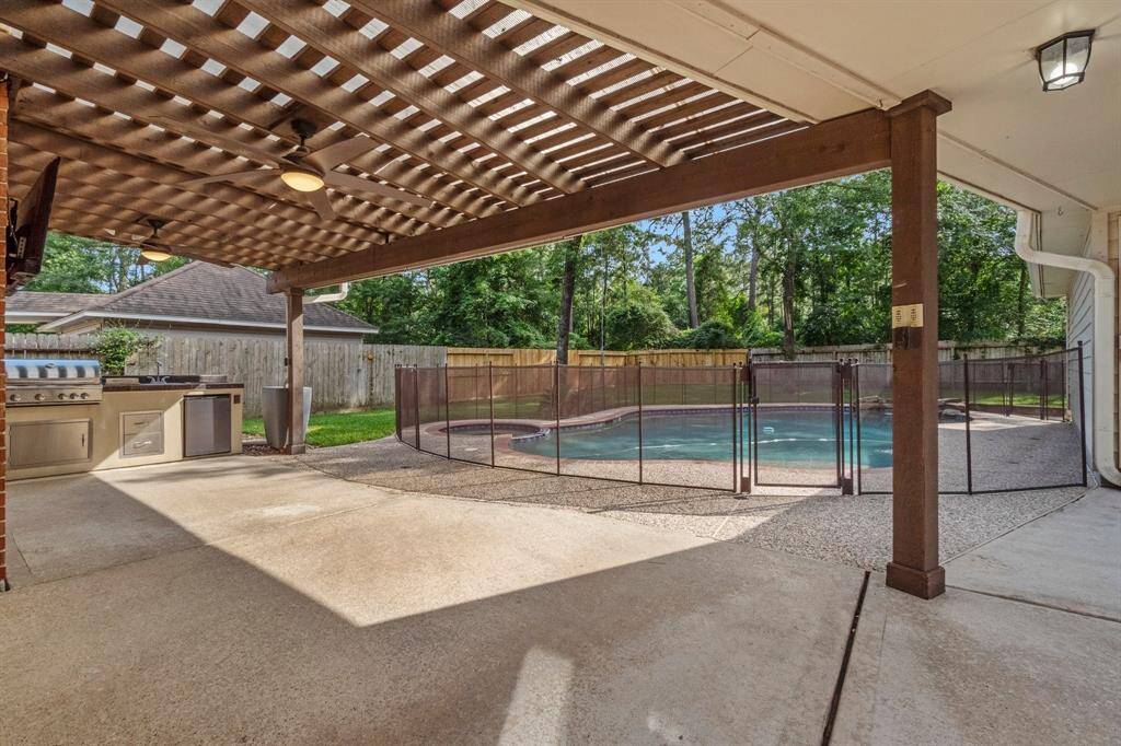 This photo showcases a spacious outdoor area with a pergola-covered patio, built-in grill, and a fenced pool, surrounded by lush greenery, perfect for relaxation and entertaining.