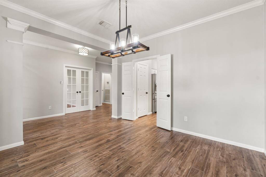 Another view of the Dining room with wood-look flooring, a modern light fixture, and neutral-painted walls offering a versatile and welcoming space.