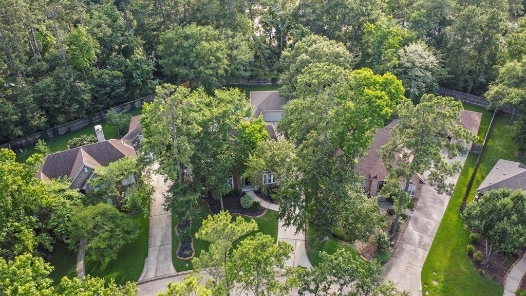 This aerial photo showcases a spacious home nestled among mature trees, offering privacy and a serene setting. The house features a large driveway and well-maintained landscaping, providing a welcoming and tranquil atmosphere.