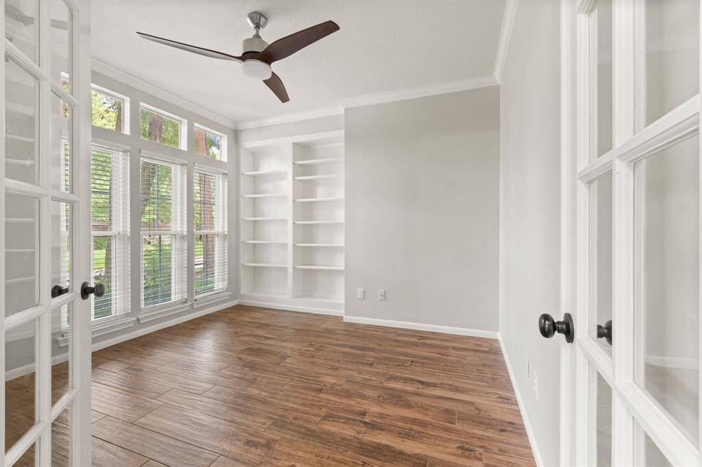 This room features large windows for natural light, a ceiling fan, built-in shelves, and elegant wood flooring, creating a bright and functional space for a home office, gym, craftroom, playroom, or whatever your needs require.