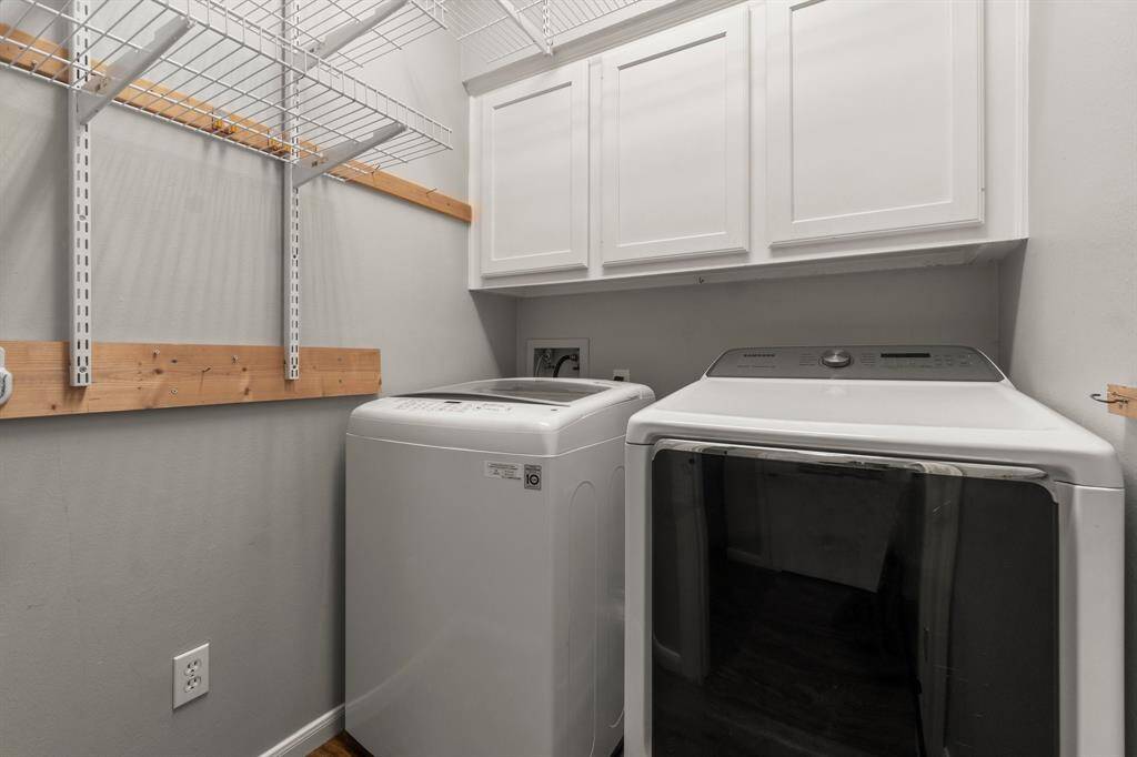 This is a compact laundry room featuring modern washer and dryer units, upper cabinets for storage, and wire shelving for additional organization.