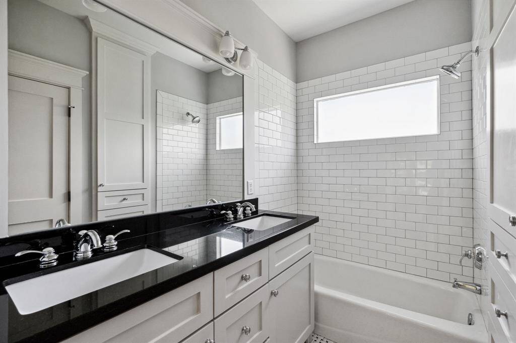 Crisp and classic with double vanity, black granite counters, and subway-tiled tub surround.