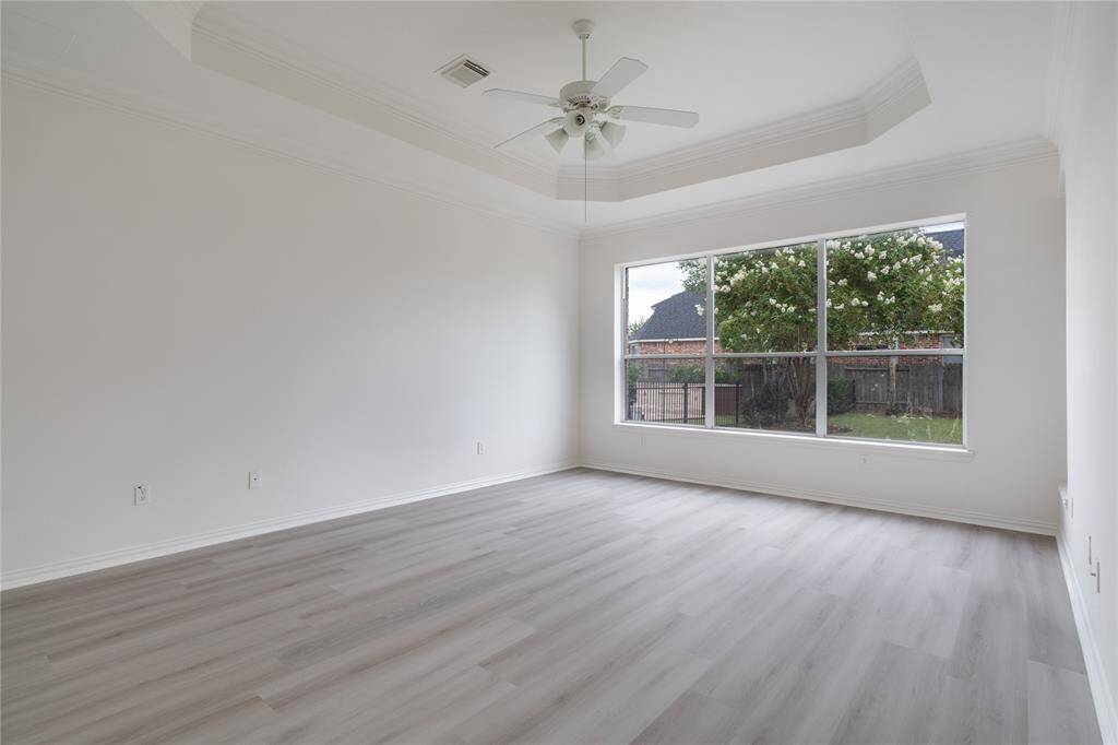 This is a bright, spacious room with modern light wood flooring, a large window offering garden views, and a ceiling fan. It has a clean, neutral color palette, ready for personalization.