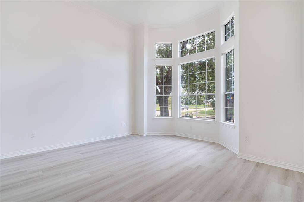 This is a bright, airy room with large windows providing ample natural light and a view of the outside. The space features modern, light wood flooring and a fresh, clean look, ideal for customization to your taste.