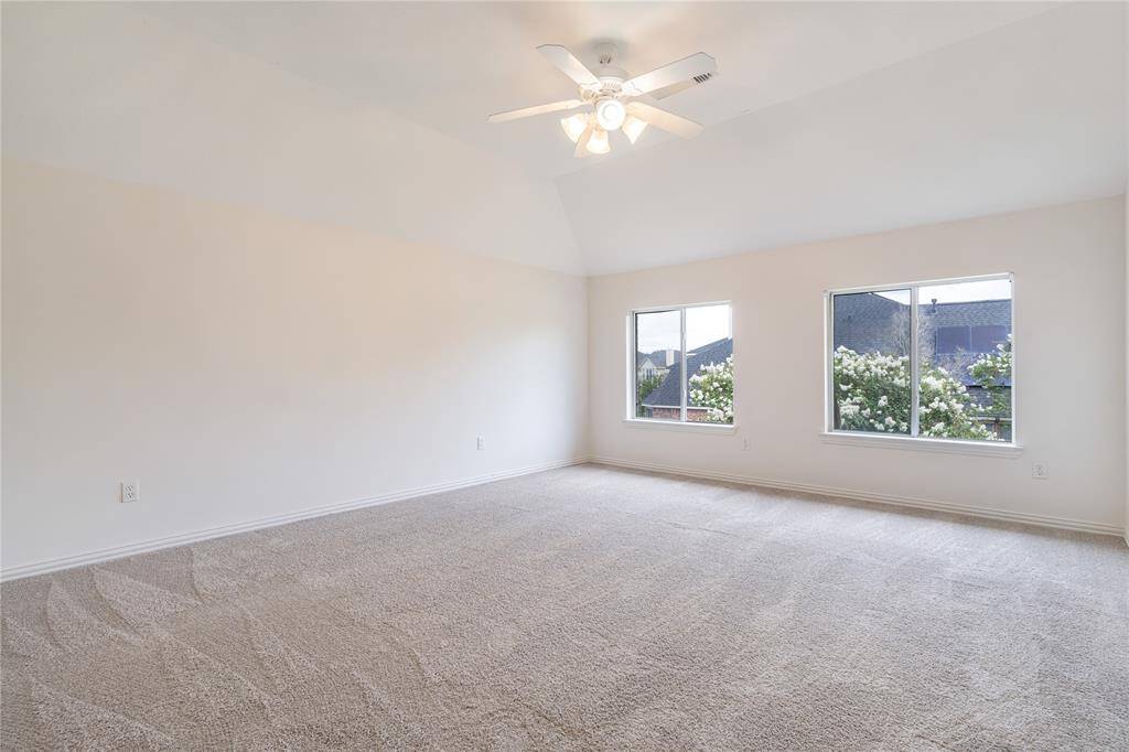 Spacious, well-lit room with plush carpeting, neutral color walls, ceiling fan, and two large windows offering garden views.