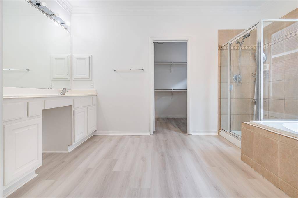 This is another angle of the bathroom featuring a large vanity with ample storage, a built-in makeup area, a spacious walk-in shower, a soaking tub, and a separate closet for additional storage.