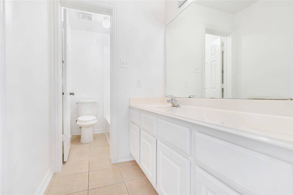 This is a bright bathroom featuring a large vanity with ample storage and a separate toilet area, complemented by neutral tiles and clean, white walls.