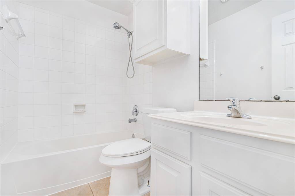 This is a bright, clean bathroom featuring a combination tub and shower with white tile surround, a single sink vanity with ample counter space, and a toilet. The space appears well-maintained with a neutral color palette.