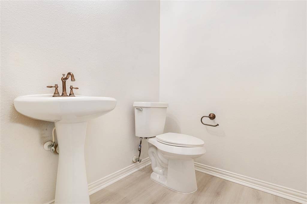 This is a clean and simple half-bath with a pedestal sink, bronze fixtures, and a toilet, featuring neutral walls and laminate flooring.