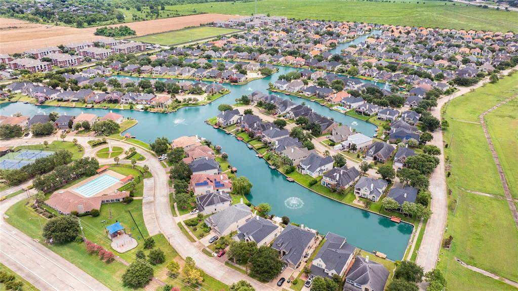 This is another angle of the aerial photo which showcases a suburban neighborhood with spacious homes along a serene, winding man-made lake, complete with community amenities such as a swimming pool and tennis courts, all set within a well-planned layout offering both privacy and communal recreational spaces.