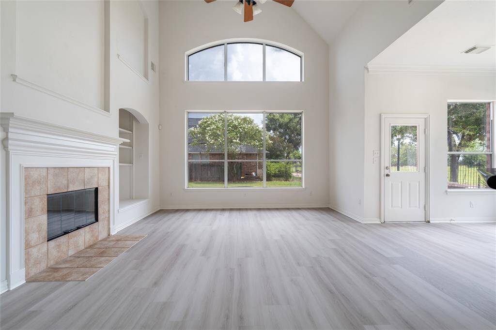 This spacious and bright living room features high ceilings, large windows, a fireplace, and modern flooring, offering a blend of natural light and comfort.