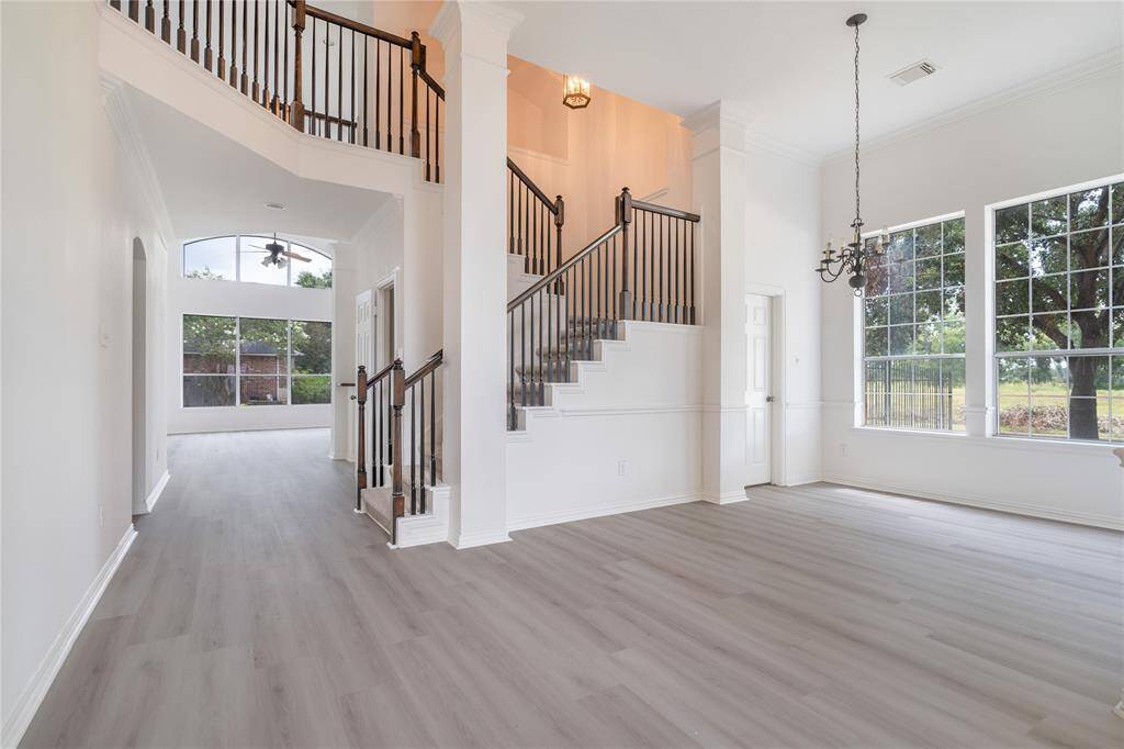 This spacious and bright two-story home interior features high ceilings, large windows for natural light, elegant grey wood flooring, white walls, and a stylish staircase with iron balusters leading to the upper level.