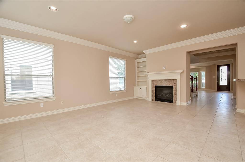Bright and airy den on a corner lot, featuring a cozy fireplace, built-ins, and tile floors, seamlessly opening to a back patio.
