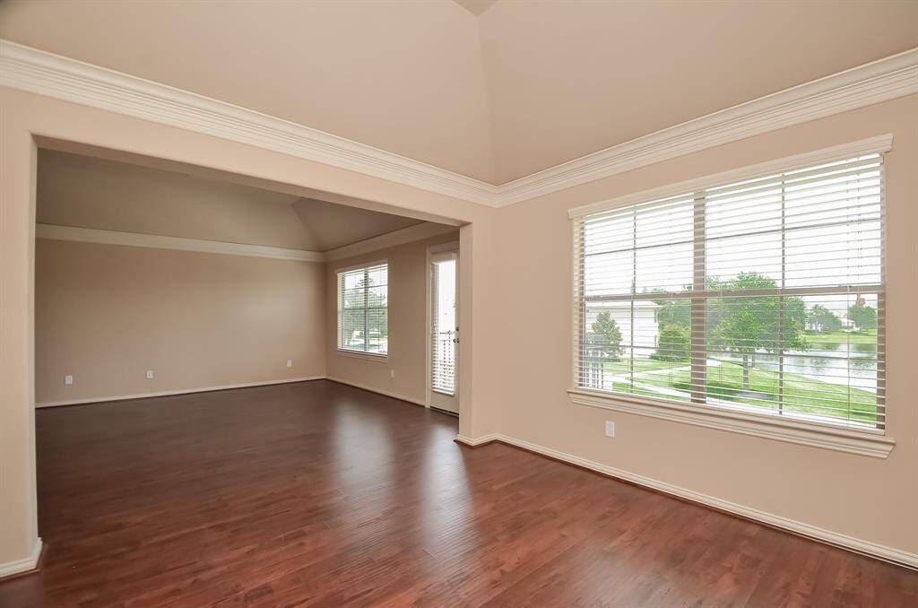 Spacious room with hardwood floors, large windows offering ample natural light and scenic outdoor views. Neutral walls and crown molding add elegance.
