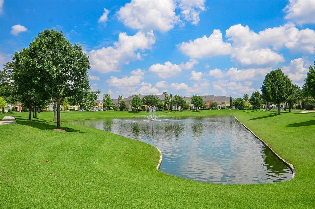 This serene neighborhood features a picturesque pond with a fountain, surrounded by lush, well-maintained green lawns and mature trees, offering a tranquil and scenic environment.