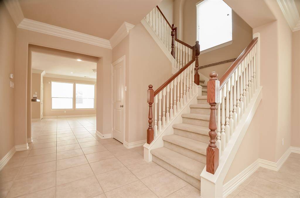 This photo showcases a spacious and bright entryway with a stylish staircase and neutral tile flooring. The open layout leads into a well-lit living area with large windows, creating an inviting atmosphere.