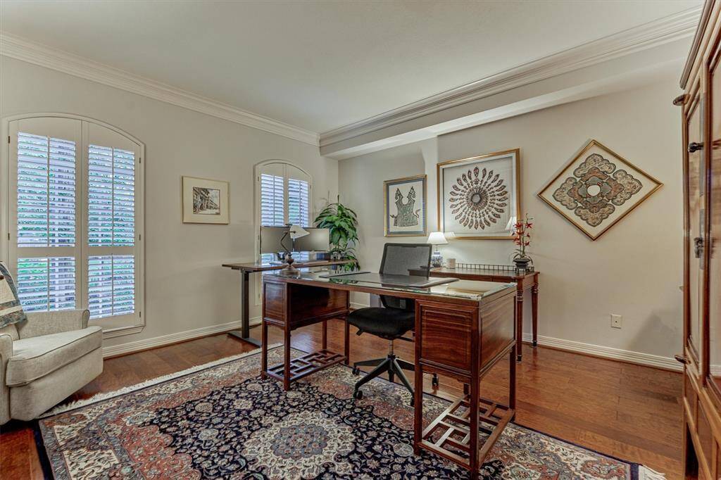 This inviting home office features hardwood floors, elegant crown molding, and ample natural light through shuttered windows, creating a warm and productive atmosphere.
