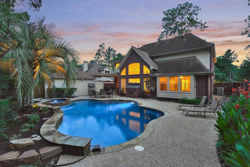 This inviting home features a beautifully landscaped backyard with a large, inviting pool and spa, surrounded by lush greenery and a spacious patio area perfect for entertaining. The warm glow from the house windows enhances the tranquil evening setting.